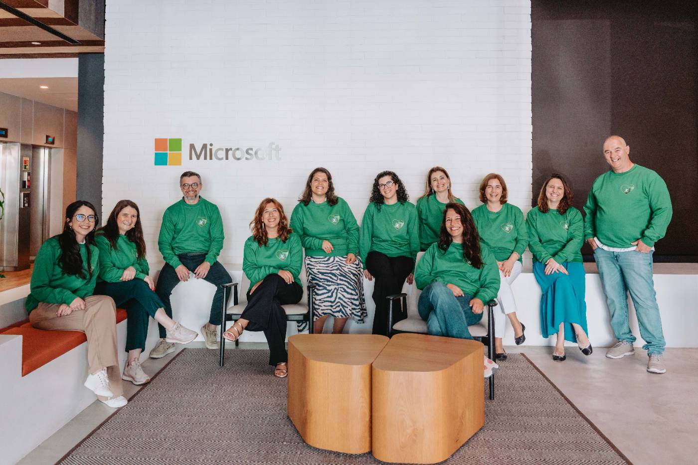 Equipa alargada de camisolas verdes reunida junto ao logótipo Microsoft